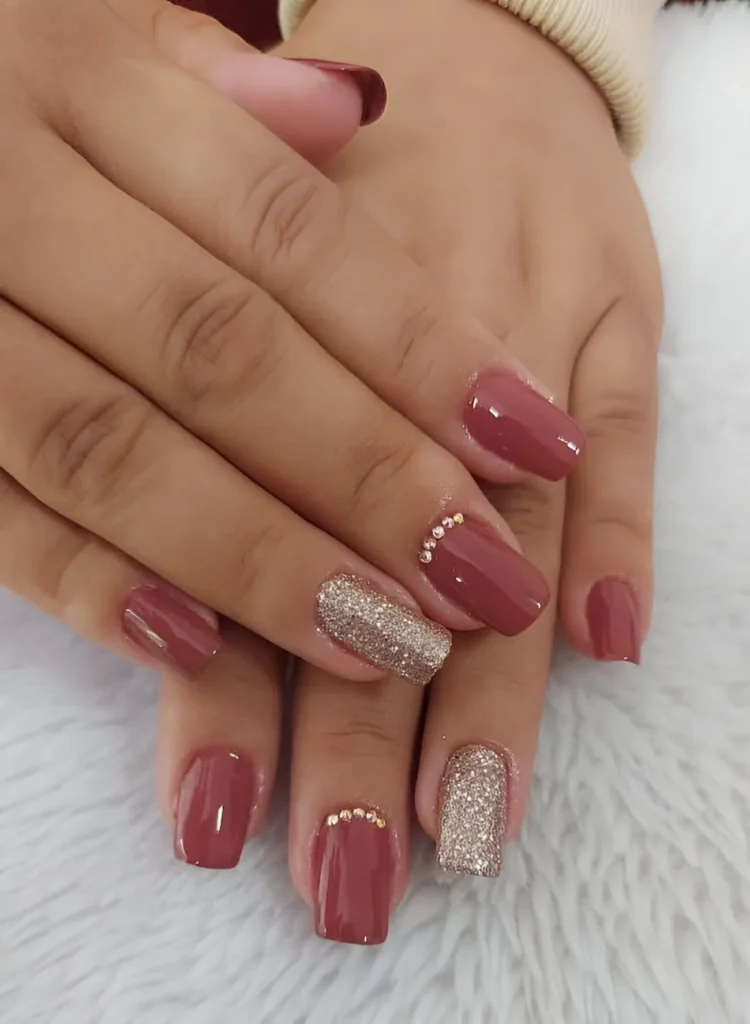 Elegant rose-toned nails with rhinestone accents and glitter.