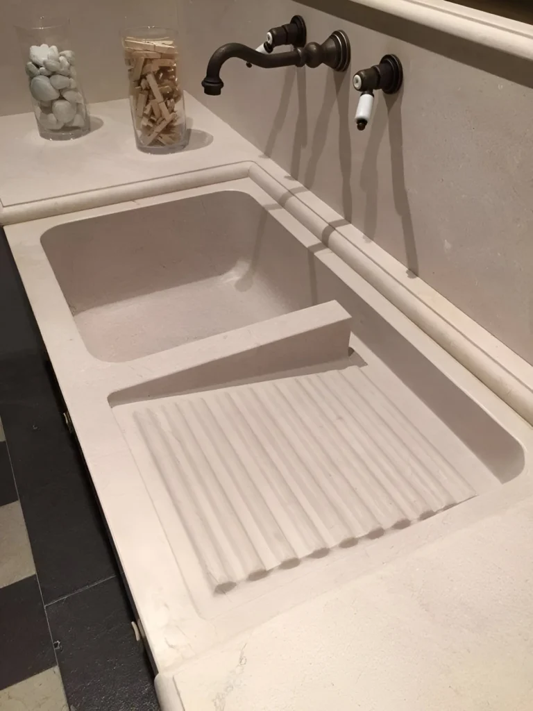 Kitchen sink with an integrated, sculpturally designed drainboard, made of a light-colored stone.