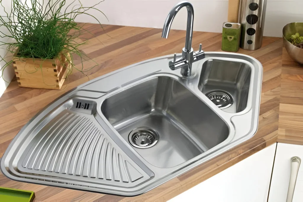 Corner kitchen sink with integrated drainboard and secondary bowl, made of stainless steel.