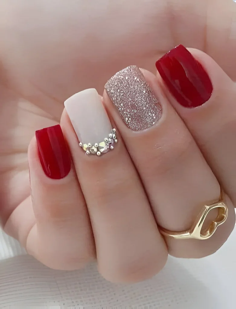 Chic red nails with glitter and rhinestone accents for a stylish look.