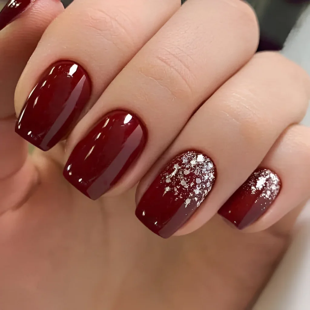 Glossy deep red nails with snowy glitter accents for a winter-inspired look.