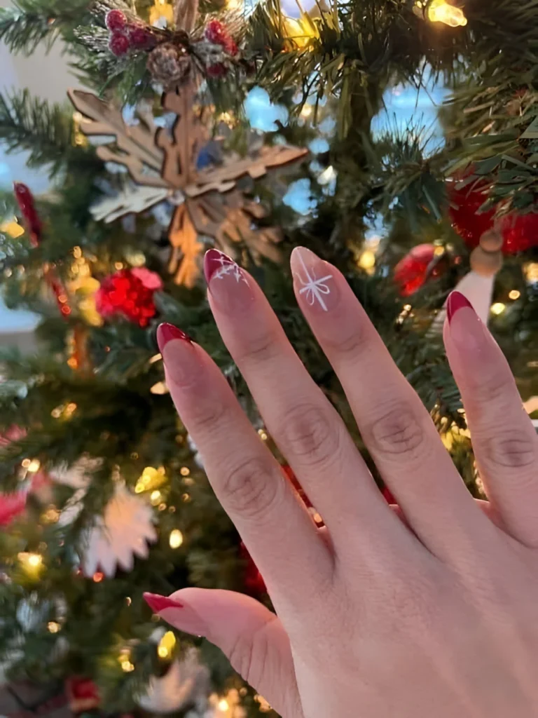 Red French tip nails with snowflake design for holidays.