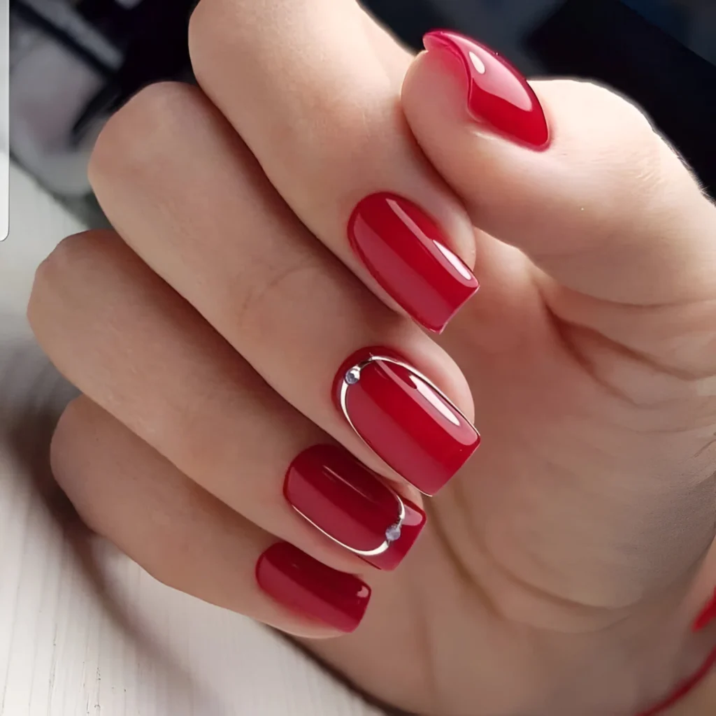 Simple red nails with silver rhinestone accent.