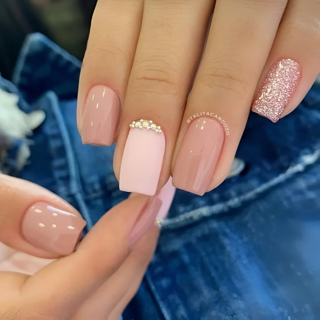 Nude and soft pink nails with pink glitter and rhinestone accents.