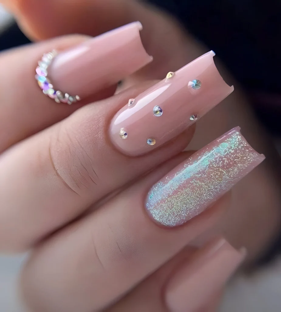 Light peach-pink nails with iridescent rhinestones and a holographic glitter accent.