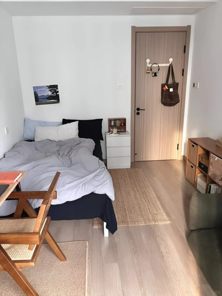 Small bedroom with light-colored wood flooring that extends to the area outside the bedroom door, creating a sense of continuous space.