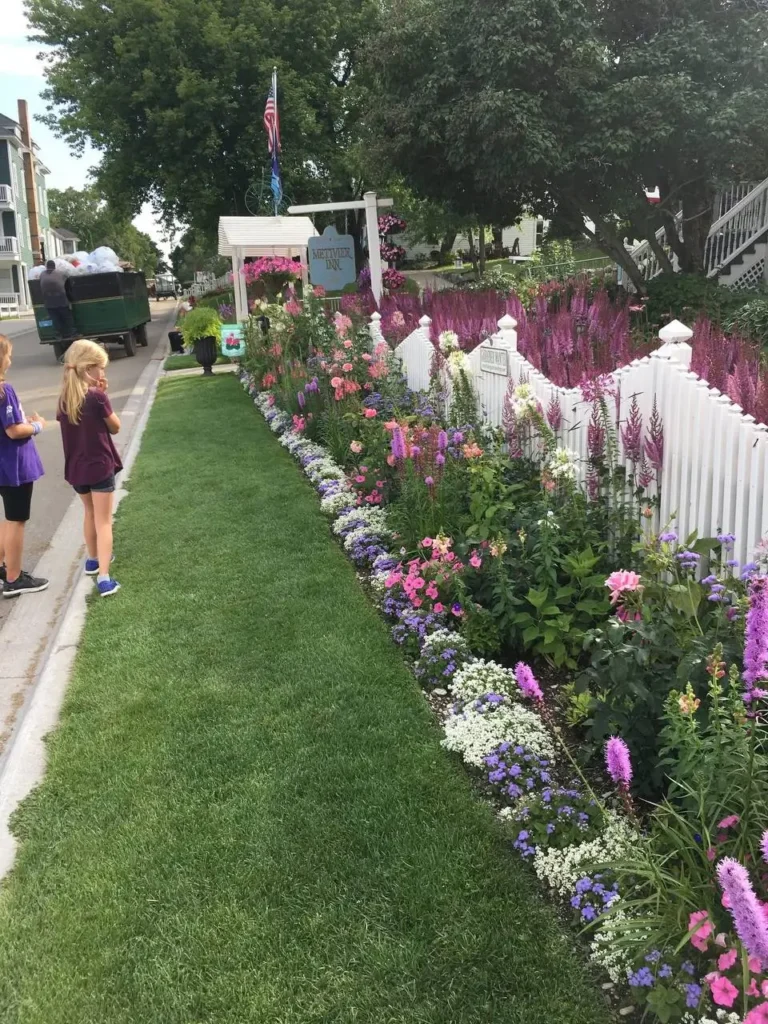 A white picket fence with a variety of colorful flowers planted along both sides, creating a charming and inviting garden border.